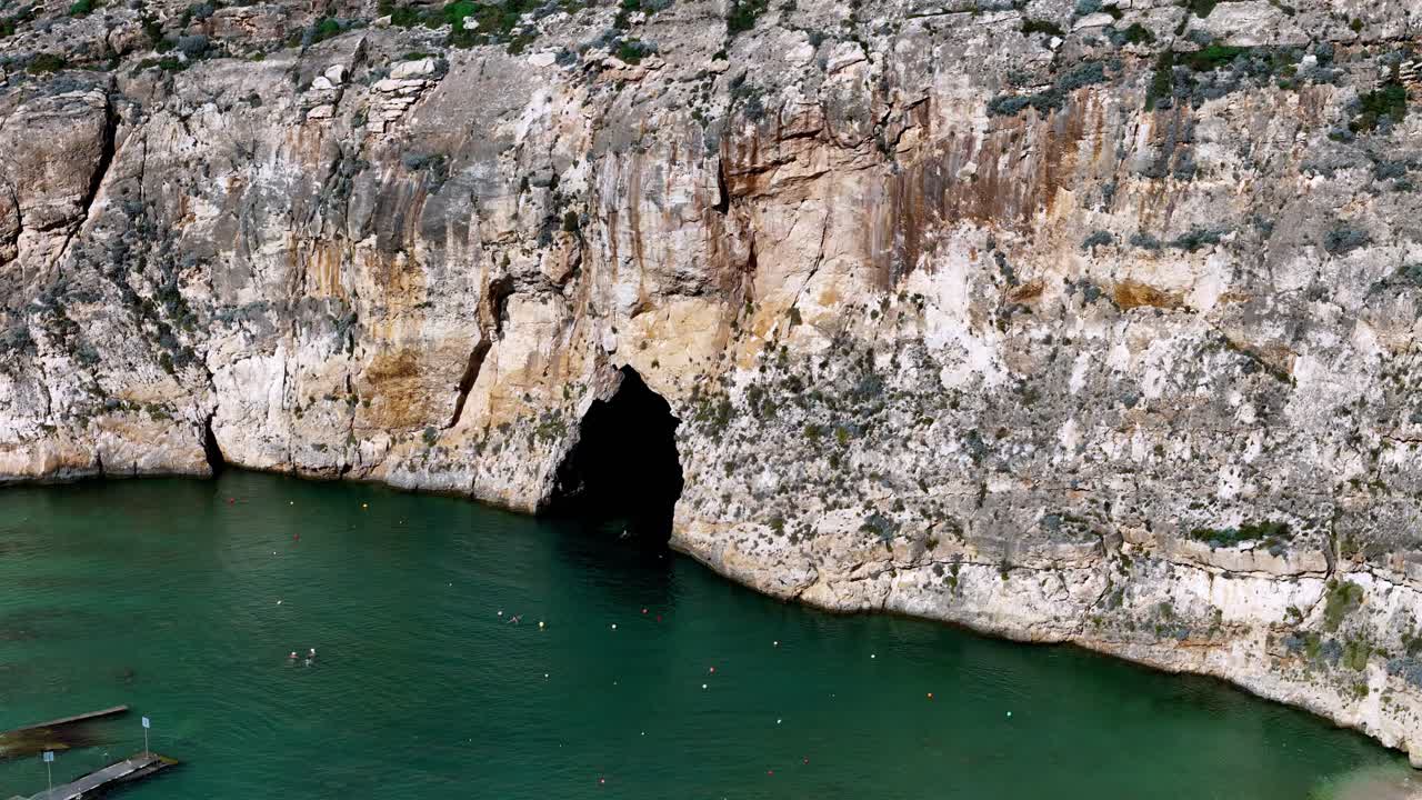 Gente nadando cerca de una gran cueva marina en Gozo, Malta