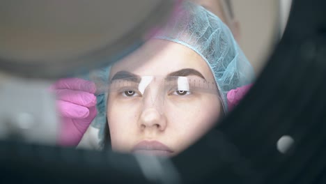 lady-in-cap-checks-brow-tattoo-with-ruler-at-large-mirror