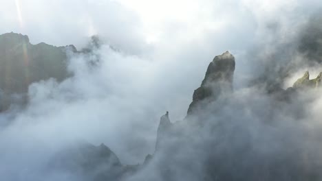 Aerial-shot-of-Pico-das-Torres-in-Madeira-with-dramatic-and-beautiful-clouds-moving-through-the-valley-and-peaks-during-sunrise-with-the-sunlight-peeking-through