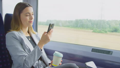 businesswoman with takeaway coffee commuting to work on train looking at mobile phone