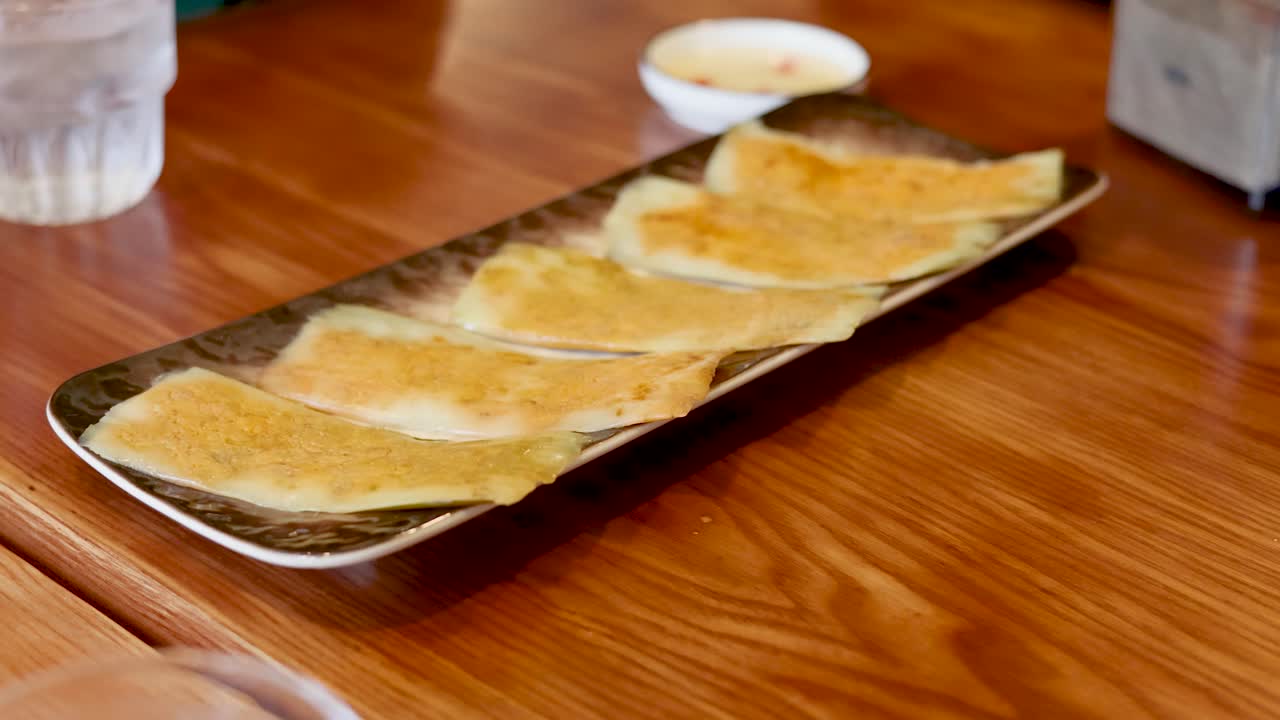 Foto close-up pancake gurih Vietnam keemasan yang tersusun di atas piring saji di atas meja kayu.