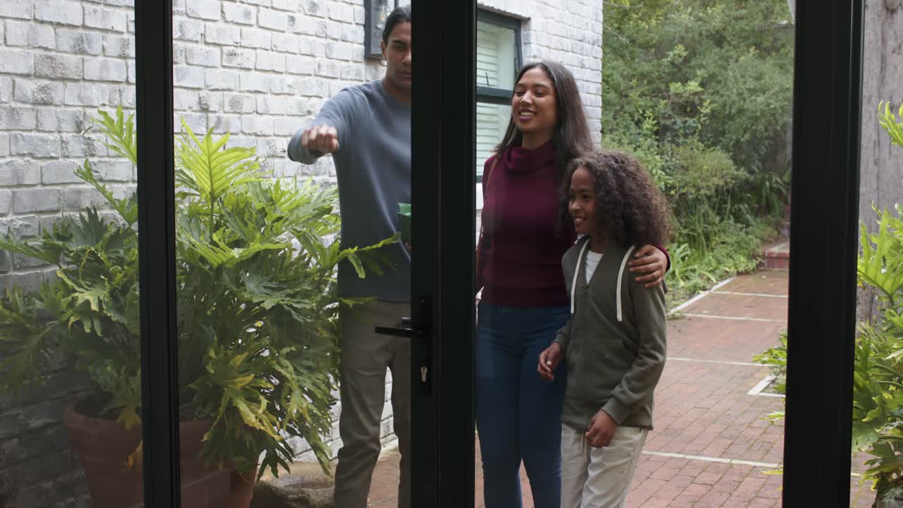 Una famiglia eterogenea si avvicina alla porta del patio con un regalo; il padre afferra la maniglia e tira la porta per entrare.