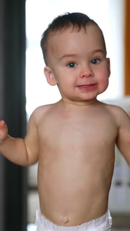 smiling caucasian baby in diaper running up to camera. lovely kid being active at home. vertical video