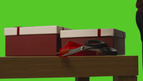 primer plano de un hombre envolviendo regalos en cajas decoradas con cinta en una mesa disparada contra una pantalla verde 1