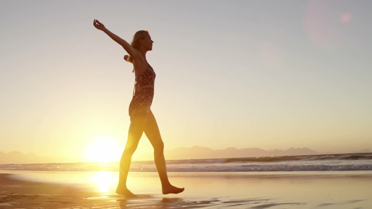Donna con le braccia distese che cammina sulla spiaggia