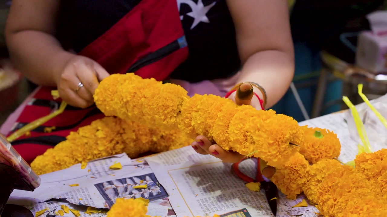 Primer plano de las manos de una mujer ensartando flores de caléndula amarillas en una guirnalda tradicional en Bangkok