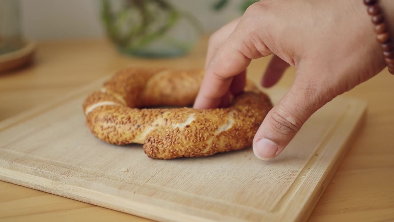 Hand Picking Up a Fresh Sesame Bagel from a Wooden Board