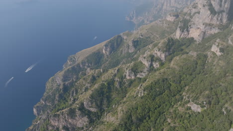 aerial footage of the mountains and cliffs off the amalfi coast with boast in the meditteranean sea