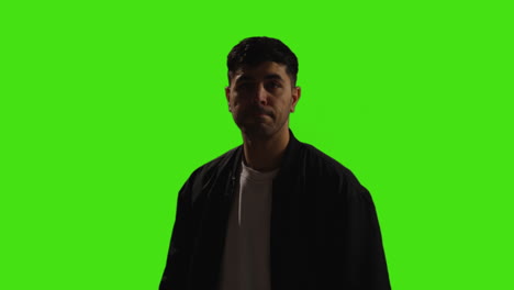 Bored-Or-Fed-Up-Young-Man-Walking-Into-Frame-Standing-And-Waiting-Against-Green-Screen-Background-With-Low-Key-Lighting