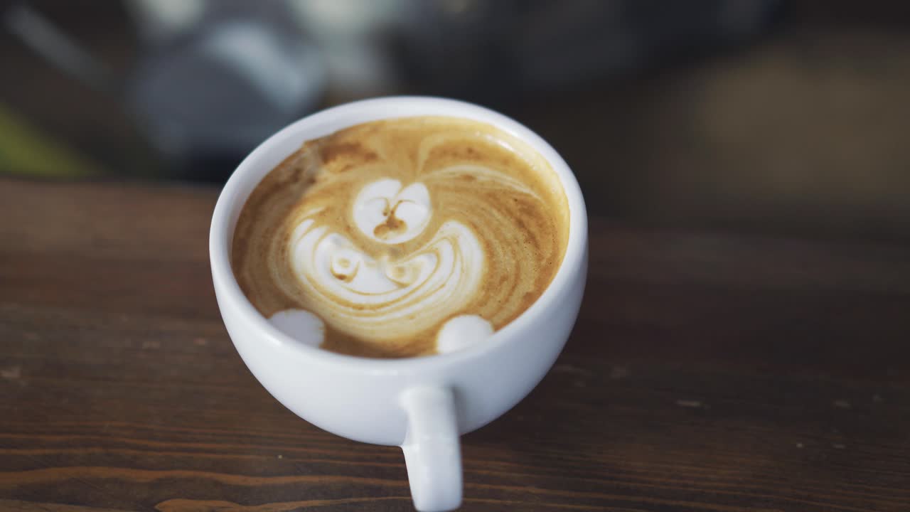 Hands of a bartender drawing with stick in a white cup of cappuccino. Process of making nice morning cappuccino coffee