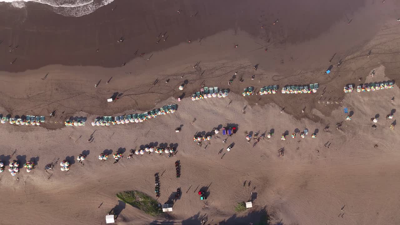 Drone scenery of a tropical beach filled with sunbathers and umbrellas, highlighting vacation life and outdoor relaxation. Aerial view of Parangtritis Beach, Yogyakarta, Indonesia