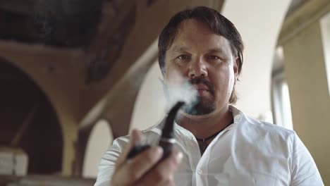 portrait of a brutal young man with a beard that smokes a pipe then offers it to the viewer close-up