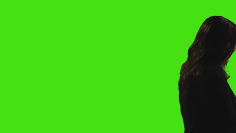 rear view silhouette of young woman standing waiting and looking around against green screen background