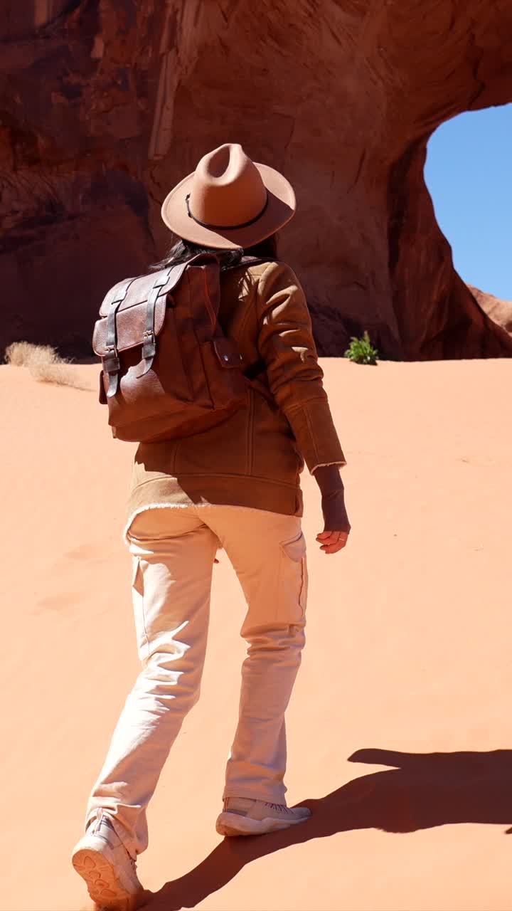 Woman with Backpack and Hat Walking Through Desert Landscape