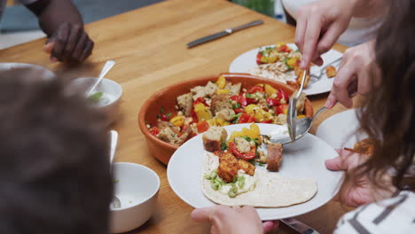 close up of man serving food to friends seated around table for dinner party