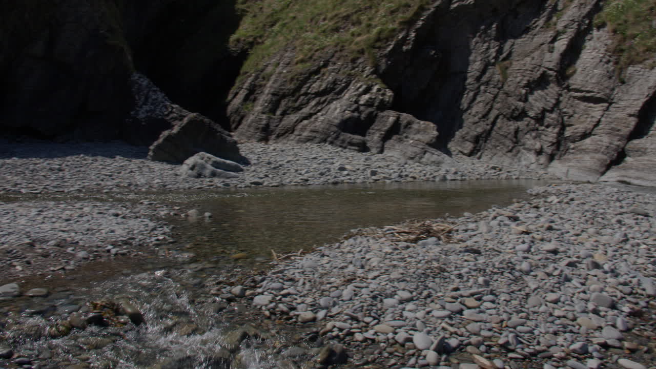 panning shot of the river Tydu flowing over pebbles and rocks on at Cwmtydu beach