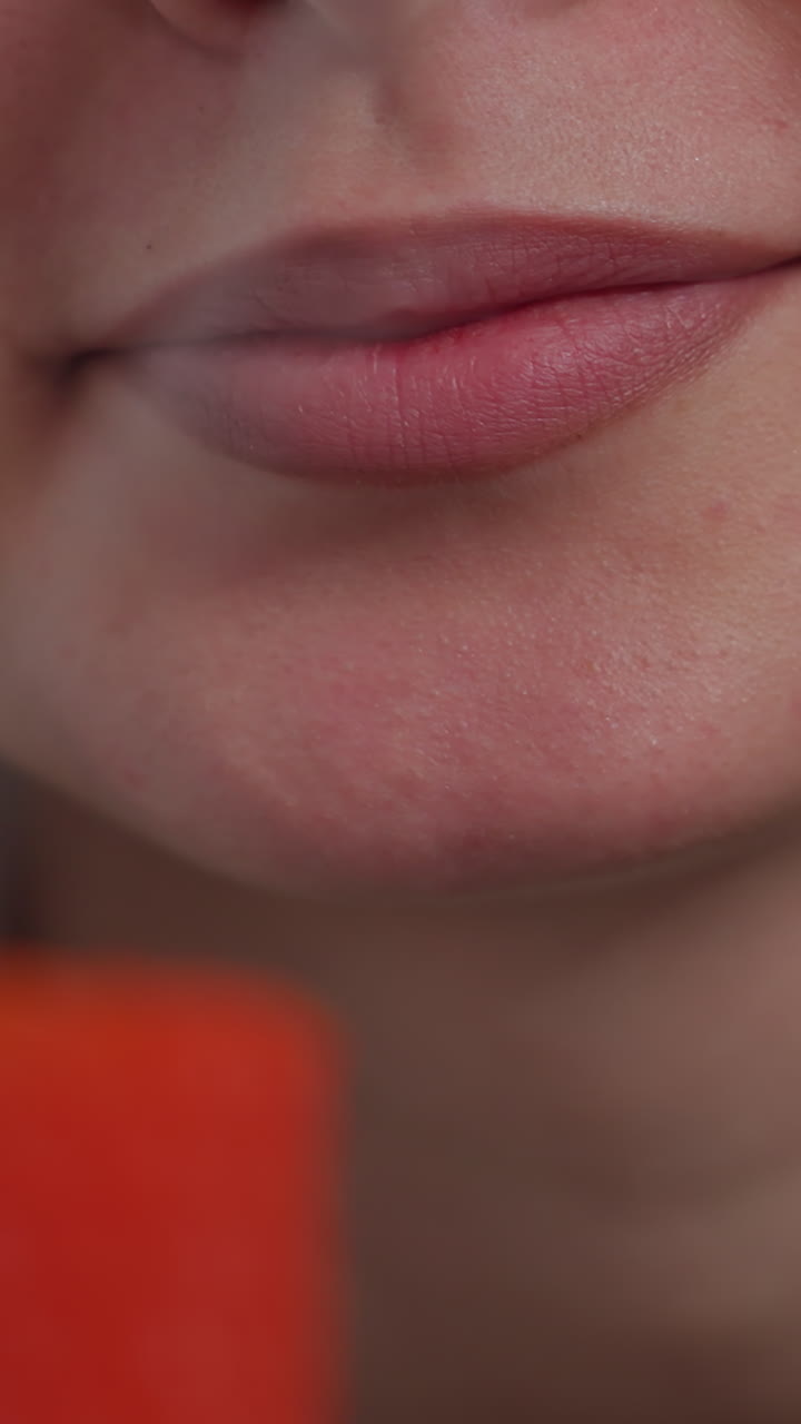 primer plano de una vela roja ardiente siendo apagada por una mujer con labios pintados, el suave resplandor de la llama contrasta con el calor de su aliento mientras se prepara para apagarla