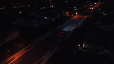 Drone-tracking-shot-of-driving-car-on-dark-street-at-night-with-orange-streetlamps