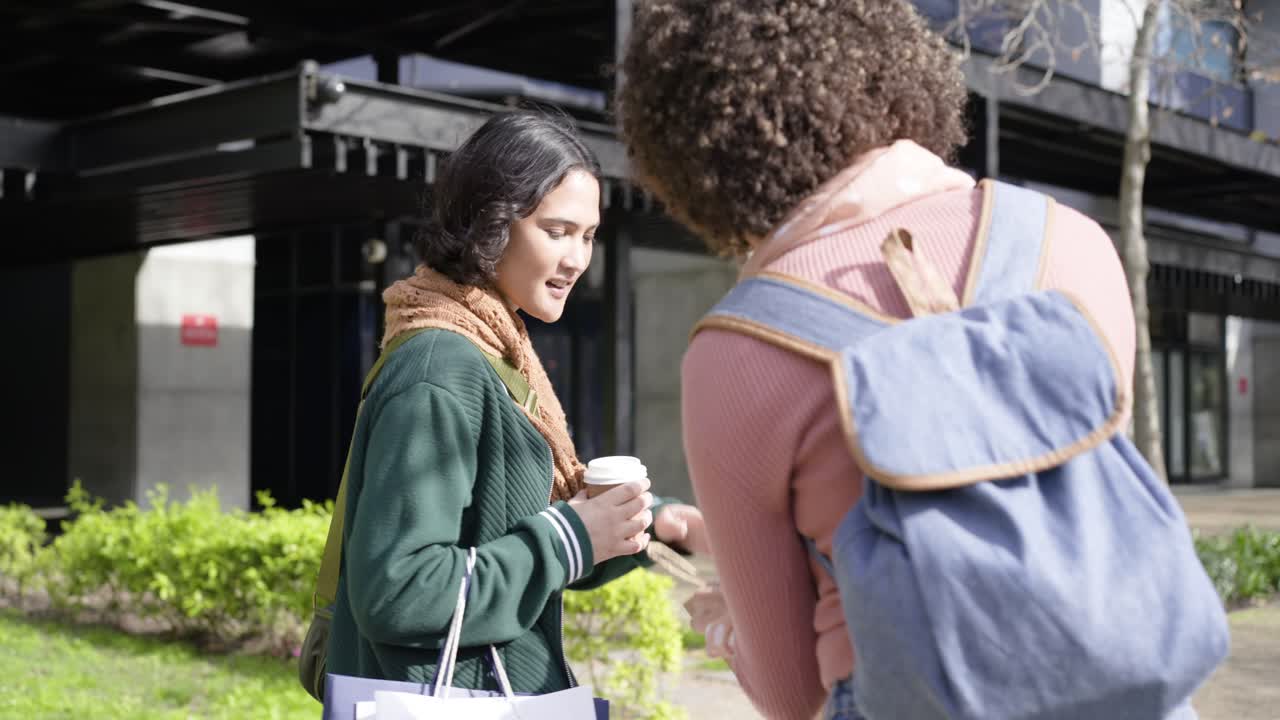 Diverse female friends meeting and exchanging coffee and gift bag at walkway celebrating friendship