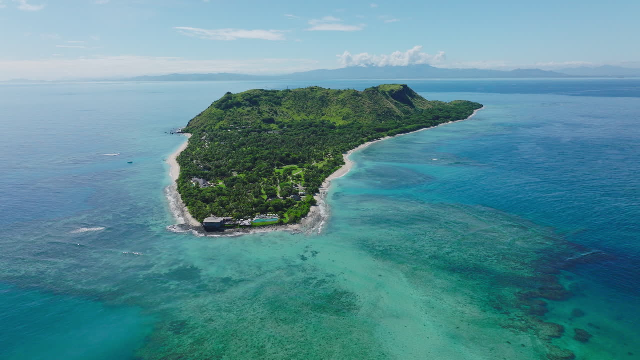 Remote tropical island seen from aerial surrounded by deep blue ocean water