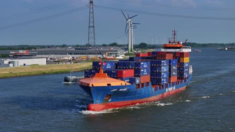 JSP-Rover-container-vessel-ship-arrives-Gravendeel,-in-the-background-we-see-the-wind-generators