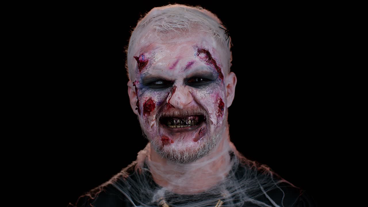 Sinister devil man with scary Halloween dead zombie makeup in costume making faces, trying to scare