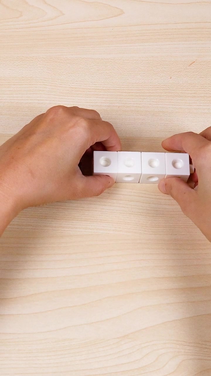 Close-up of hands assembling white and brown interlocking plastic cubes on a light wood table.