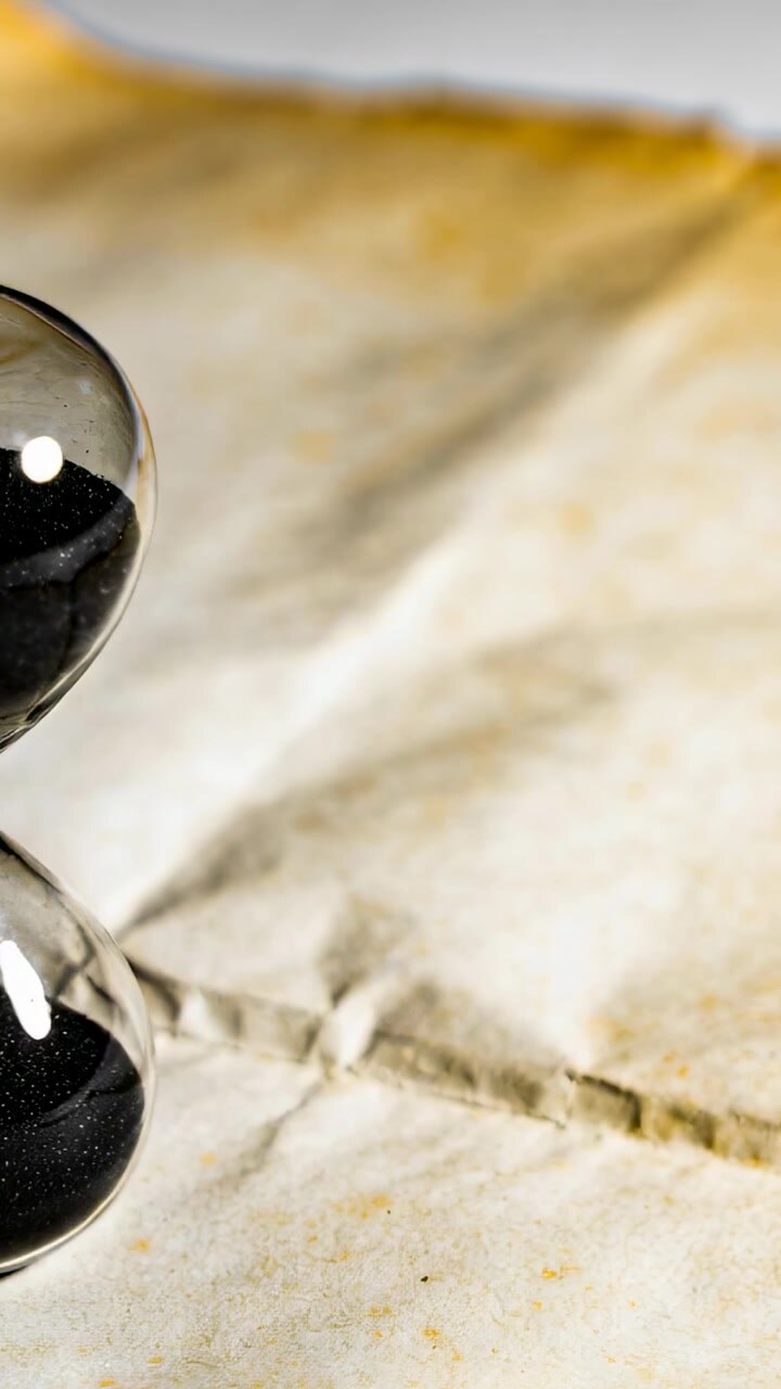 Vertical video: Shifting light casting glints on glass orbs on tabletop parchment, copy space