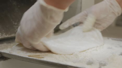 las manos con guantes del panadero frotan la harina en cada pastel antes de hornearlo. el cocinero aplica la harina a las piezas de masa para hornear lavash. primer plano.