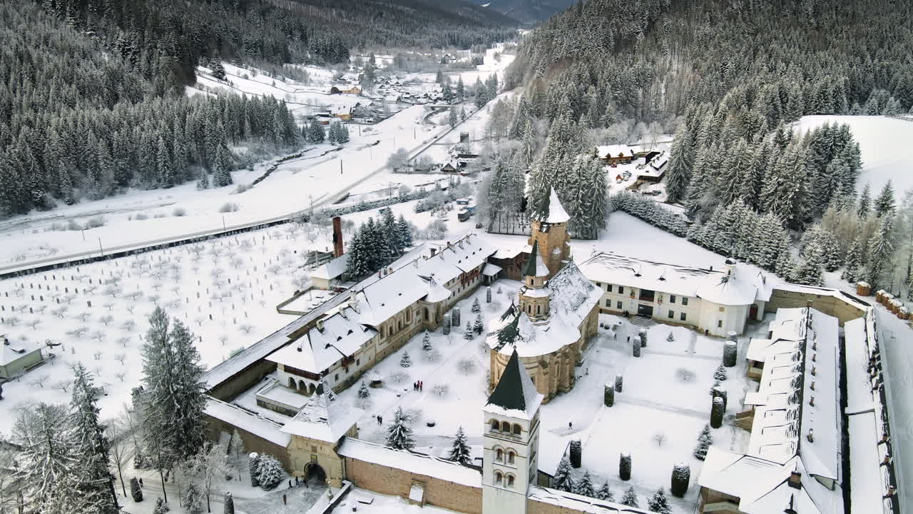 Vista aerea con drone del Monastero di Putna in inverno, Romania. Cortile interno, alberi spogli, neve, colline circostanti, valle