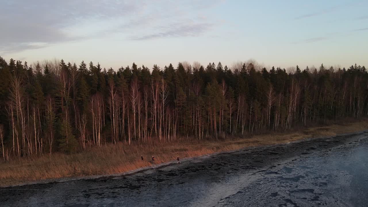 3 personas patinando sobre hielo en un lago salvaje congelado junto a un bosque durante la puesta de sol en letonia