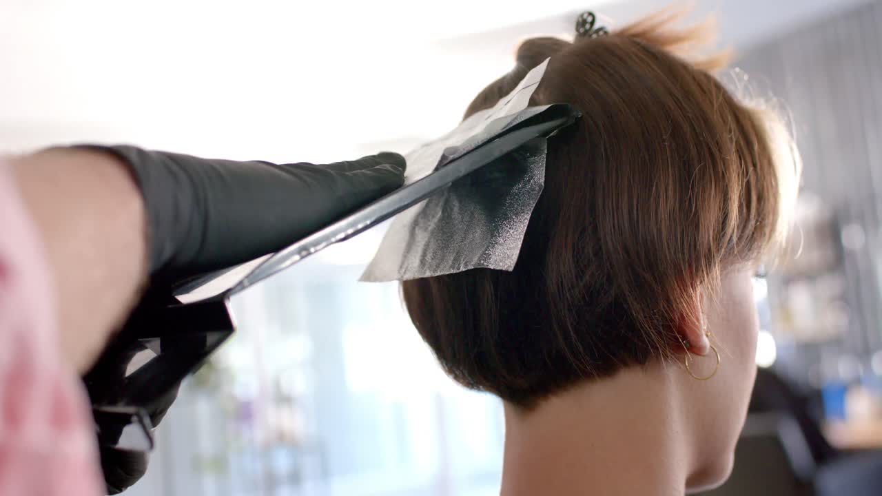 Hands of hairdresser using foil for highlighting client's hair at hair salon, in slow motion