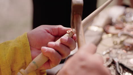 an extreme close-up shot shows an artisan's hands creating a historic replica ring. the jeweler uses a small hammer to shape the metal wire around a wooden mandrel