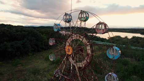 Aerial-Closeup-of-Colorful-sunset-ferris-wheel-in-abandoned-Japanese-Theme-Park-Kejonuma-Leisure-island,-panoramic-skyline-in-overgrown-green-asian-fields