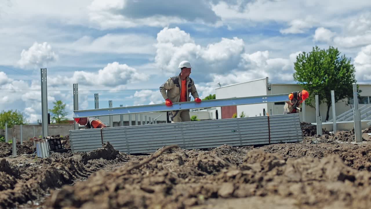 Construction solar farm. Workers in protective uniform build metal basis on the ground in summer day. Slow motion.