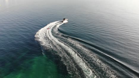 following aerial tracks child tubing behind powerboat in clear water