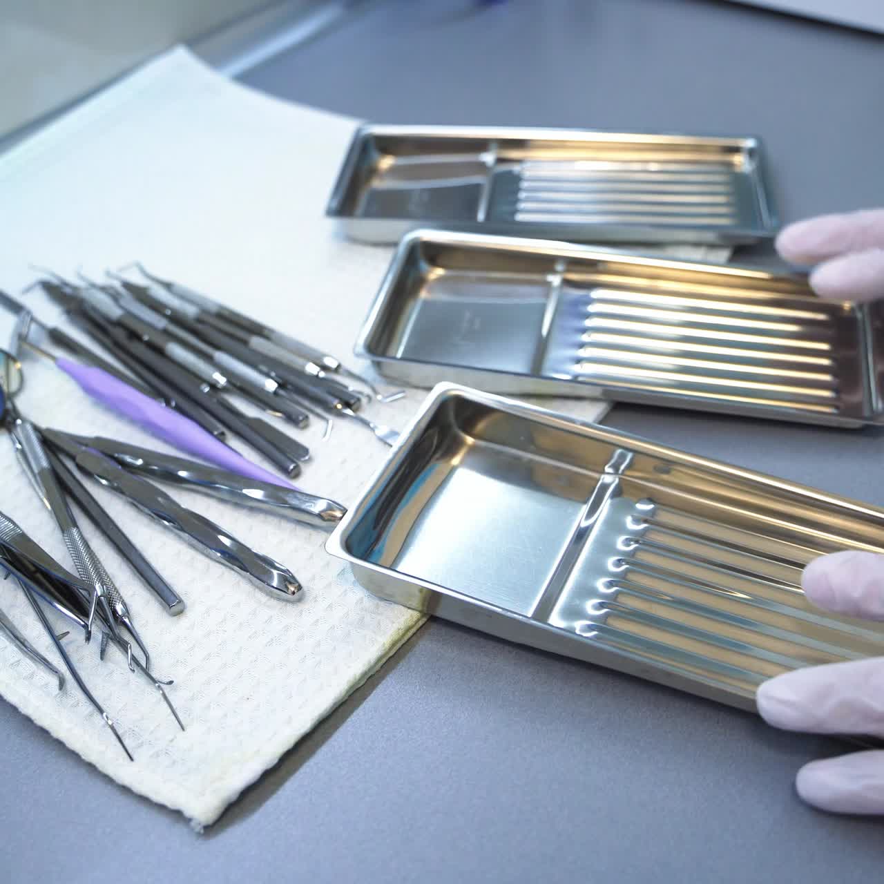Hands in glove put the dental instruments on a little metal trays. Medical staff preparing tools for stomatology examination. Close up