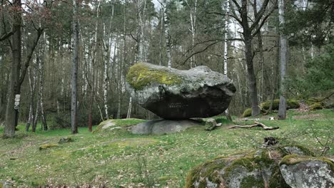 Drone-circling-around-a-sliding-rock-in-a-forest-clearing-with-grass,-daytime,-no-people