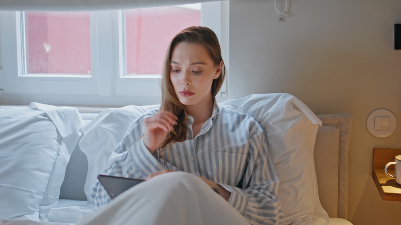 Resting lady holding cup coffee in cozy bedroom looking tablet screen closeup