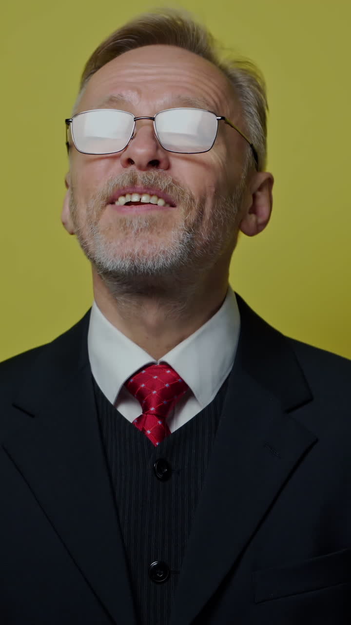 Portrait of smiling businessman on yellow background. Mature man in costume with tie talking and looking on camera. Vertical video