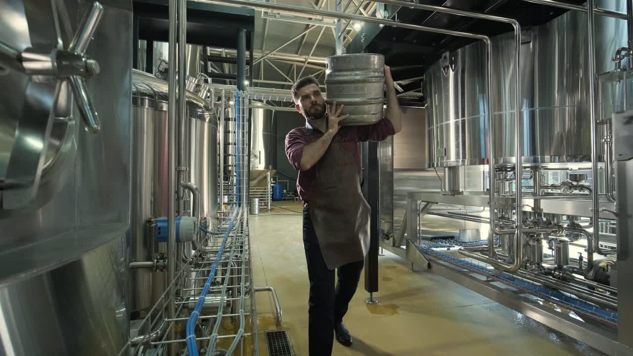 un joven cervecero con un delantal de cuero lleva un barril de cerveza artesanal en una cervecería moderna