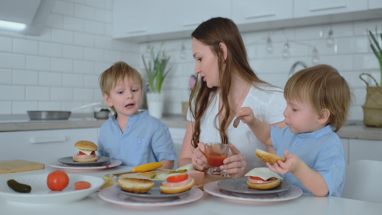 madre joven con dos hijos pequeños en la cocina en la mesa preparando una hamburguesa para el almuerzo