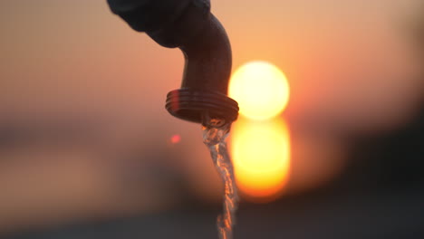 Wasser-Fließt-Aus-Dem-Wasserhahn-Vor-Dem-Hintergrund-Des-Sonnenuntergangs