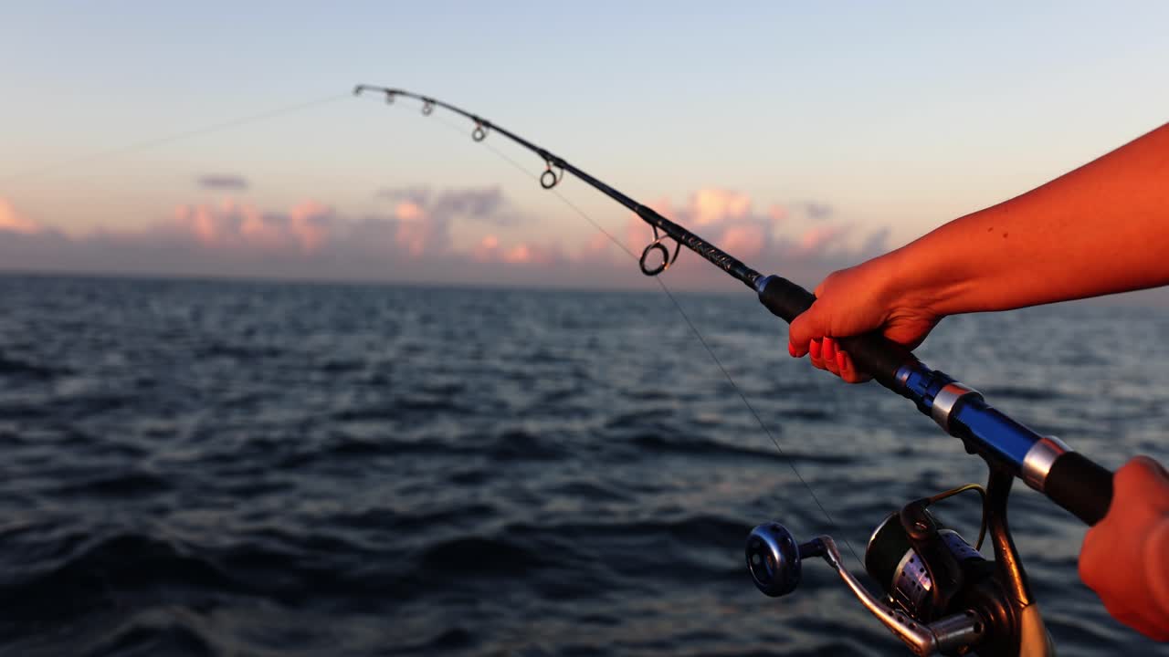 Mano che tiene una canna da pesca al tramonto sull'oceano