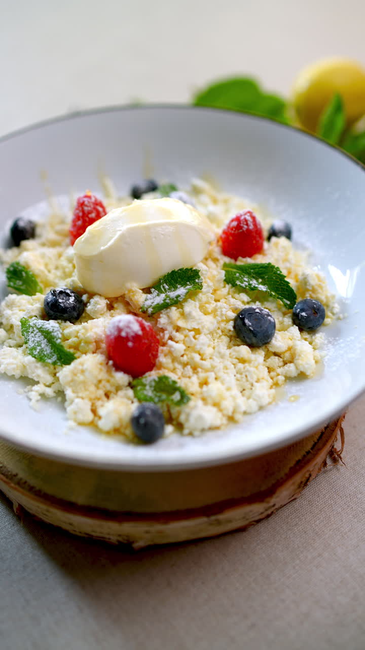 Creamy granular cheese dessert drizzled with golden honey, garnished with vibrant berries and mint, served alongside smooth ice cream on white plate