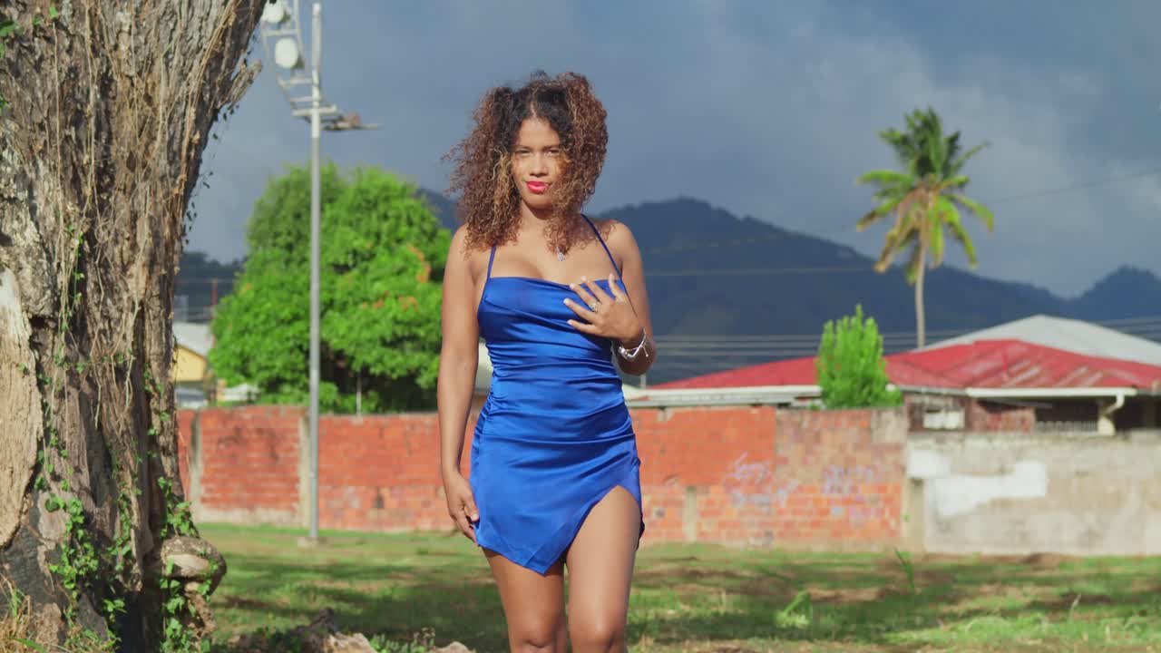 짧은 파란색 드레스를 입고 곱슬머리를 가진 어린 소녀가 카리브해의 트리니다드 섬의 열대 공원을 즐기고 있습니다.