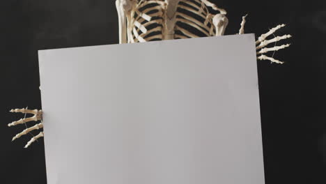 video of close up of halloween skeleton holding white board with copy space on black background