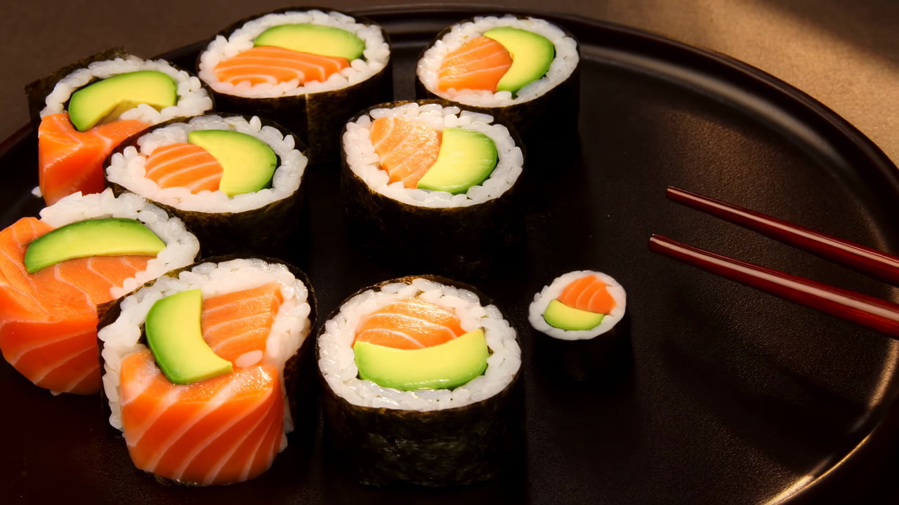 Sushi Rolls On Black Plate, Salmon And Avocado Maki Arranged Beside Red Chopsticks, Warm Lowkey Lighting,