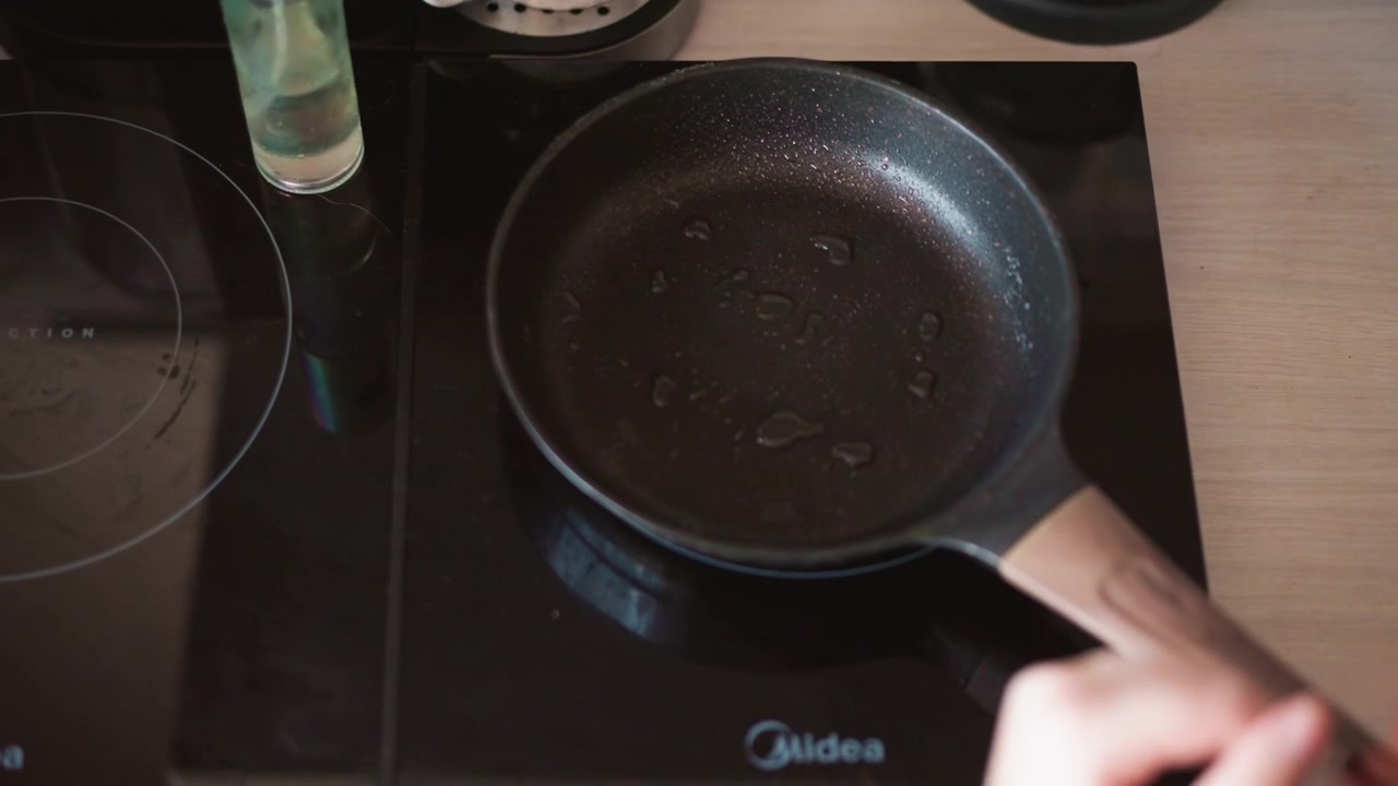 Empty frying pan on stovetop, closeup nonstick skillet with oil droplets, home cook preparing breakfast with gentle hand movement, warm kitchen light creating cozy atmosphere, subtle ritual tone