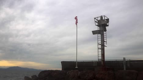 Stetige-Aufnahme-Einer-Amerikanischen-Flagge,-Die-Im-Windnetz-Zu-Einem-Wachturm-Im-Meer-Weht